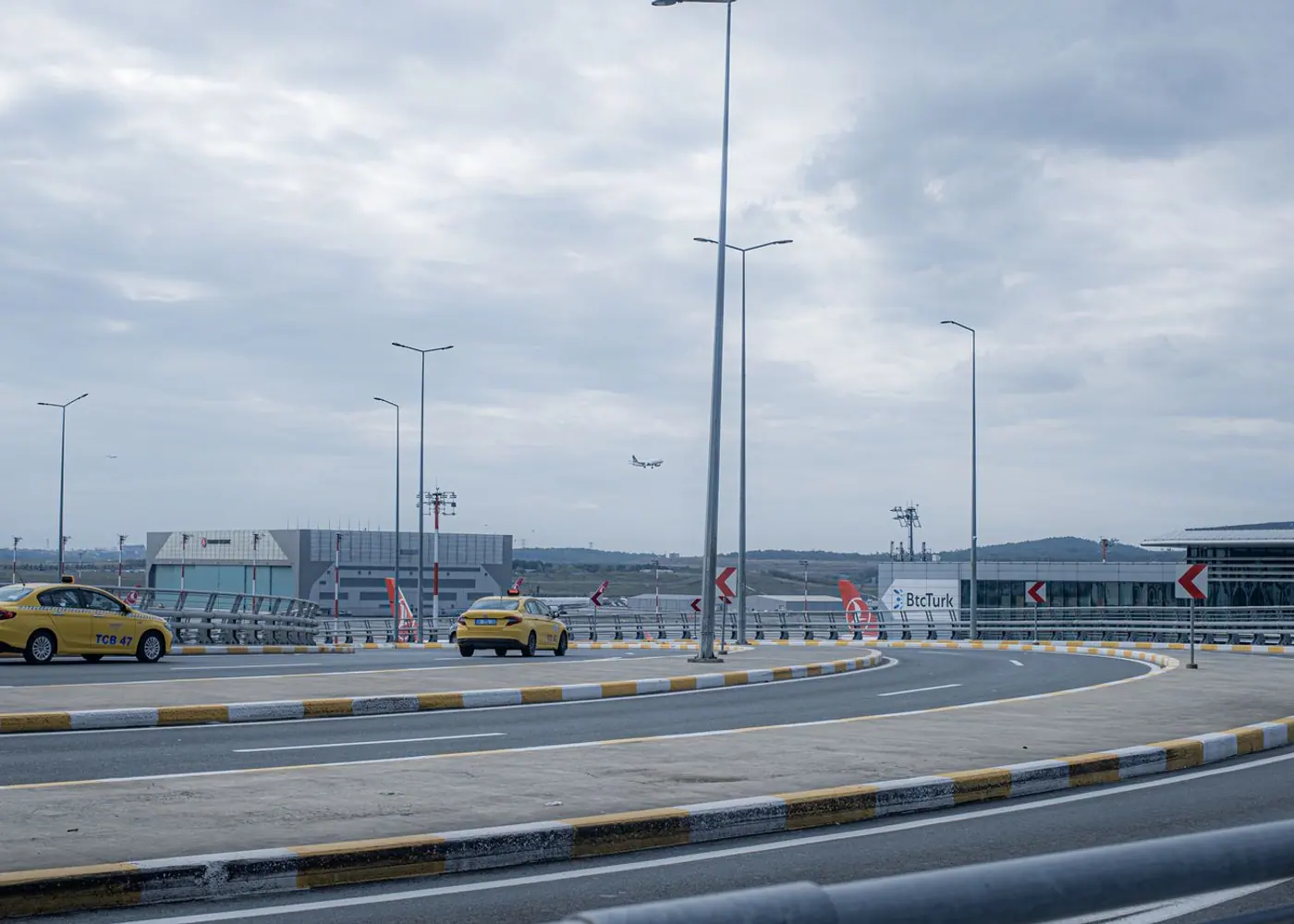 Taxis on an airport approach road with an aircraft landing in the distance